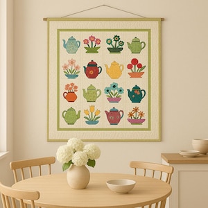 May include: A wall hanging with a grid pattern of illustrated teapots and floral displays. The artwork is framed with a green border and suspended from a wooden rod. The colour scheme includes green, red, yellow, and blue.