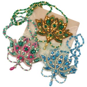 May include: Three beaded lotus flower necklaces in shades of green, pink, and blue. Each necklace features intricate beadwork and dangling accents. The necklaces are displayed on a neutral background, showcasing the detailed craftsmanship.