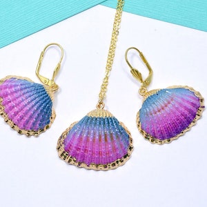 Może przedstawiać: Zestaw złotych kolczyków i naszyjnika z iryzującymi różowymi i niebieskimi muszelkami. Muszelki mają fakturowaną, iryzującą powierzchnię.