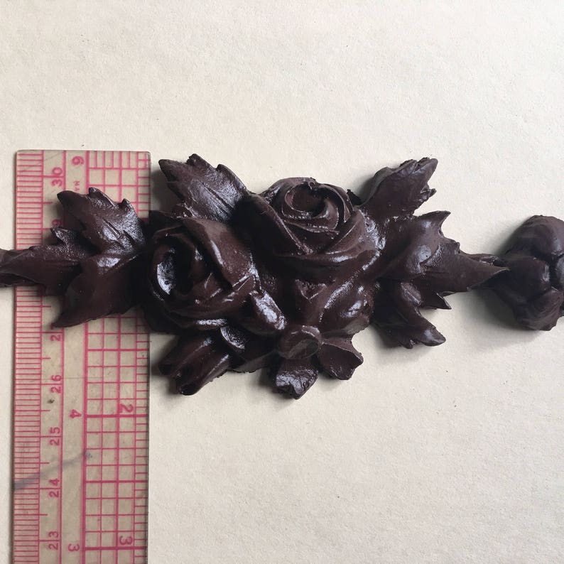 May include: A dark brown, decorative, floral-shaped ornament with a cluster of roses and leaves. The ornament is approximately 6 inches long.