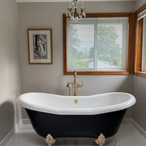 May include: A black clawfoot bathtub with gold accents sits on a white marble floor in a bathroom with a white ceiling and gray walls. A crystal chandelier hangs from the ceiling.