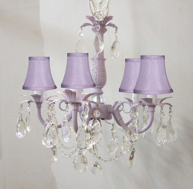 May include: A lavender chandelier with five light bulbs and crystal accents. The chandelier has a traditional design with a central stem and five arms that extend outwards. Each arm has a lavender fabric lampshade and a crystal pendant.