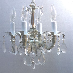 May include: A white, metal chandelier with crystal drops. The chandelier has four light bulbs and a chain hanging from the ceiling.