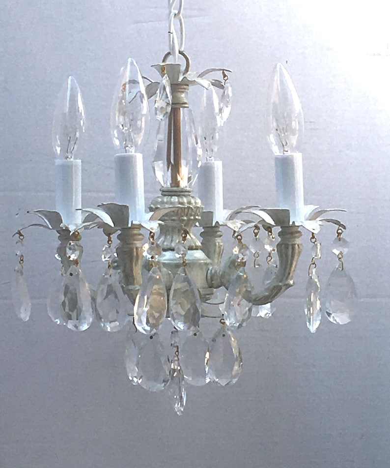 May include: A white, metal chandelier with crystal drops. The chandelier has four light bulbs and a chain hanging from the ceiling.