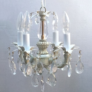 May include: A white metal chandelier with crystal drops. The chandelier has four candle-style light bulbs and a white cord.