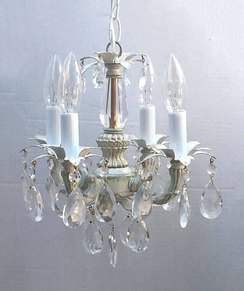 May include: A white metal chandelier with crystal drops. The chandelier has four candle-style light bulbs and a white cord.