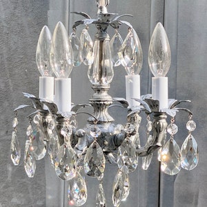 May include: A silver chandelier with crystal drops and four candle-style light bulbs. The chandelier has a distressed, aged look.