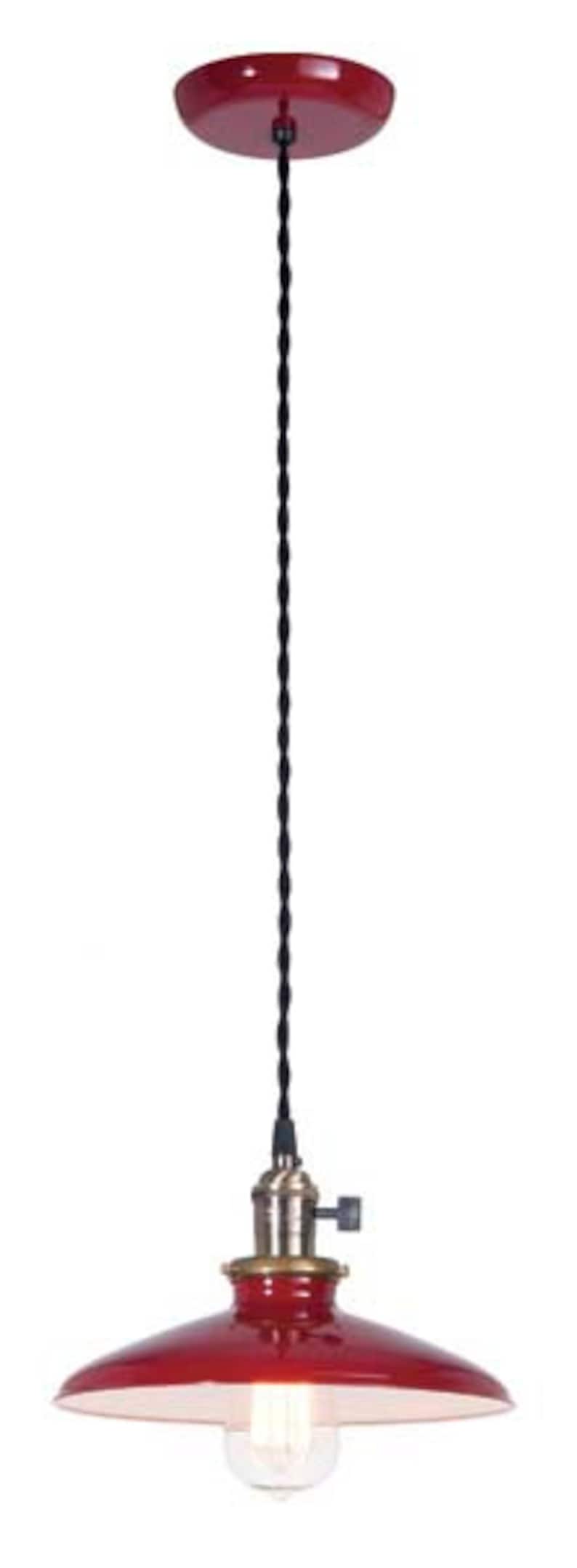 Puede incluir: L&aacute;mpara colgante roja con un cable negro y una toma de lat&oacute;n. La luz tiene una pantalla de metal roja con un interior blanco.