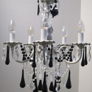 May include: A silver chandelier with black and clear crystal drops. The chandelier has five light bulbs and a decorative top.