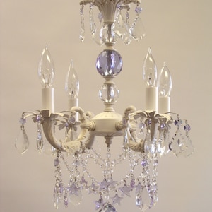 May include: A white chandelier with crystal drops and purple accents. The chandelier has a star-shaped design and is perfect for a bedroom or dining room.
