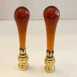 May include: Two amber glass and brass bottle stoppers with a teardrop shape.