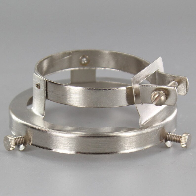 Puede incluir: Un adaptador de casquillo de bombilla de metal plateado con una abrazadera para sujetarlo a una superficie. El adaptador tiene dos tornillos para asegurar la abrazadera.