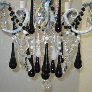 May include: A white chandelier with black teardrop-shaped crystals hanging from it. The chandelier has a white and gray finish and is decorated with black beads.