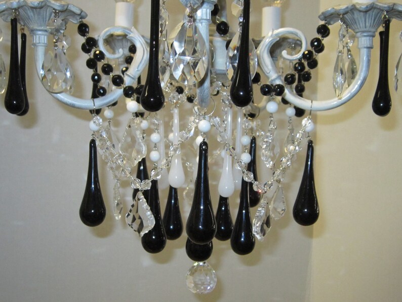 May include: A white chandelier with black teardrop-shaped crystals hanging from it. The chandelier has a white and gray finish and is decorated with black beads.