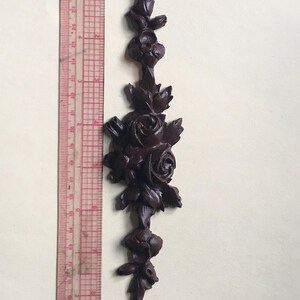 May include: A dark brown wooden decorative piece with a carved design of roses and leaves. The piece is about 7 inches tall.