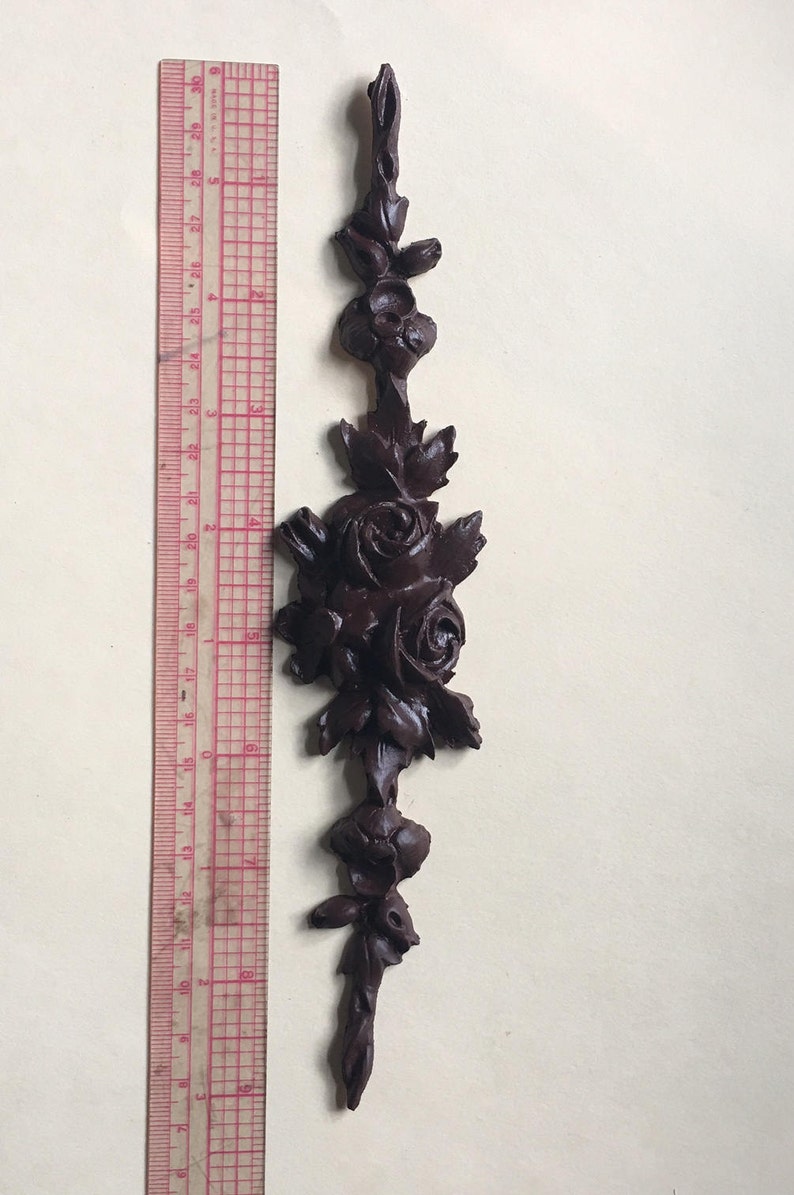 May include: A dark brown wooden decorative piece with a carved design of roses and leaves. The piece is about 7 inches tall.