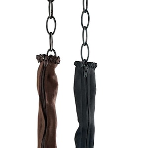 Może przedstawiać: Dwa rozciągające do butów wykonane z tkaniny, wiszące na łańcuchach. Jeden jest brązowy, a drugi czarny. Oba mają zamek błyskawiczny pośrodku.