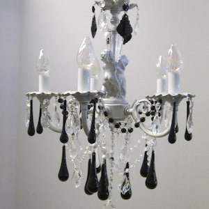May include: A white chandelier with black teardrop crystals. The chandelier has five light bulbs and a decorative metal top.
