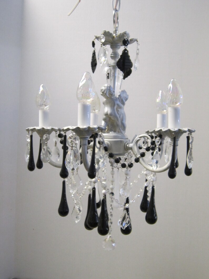 May include: A white chandelier with black teardrop crystals. The chandelier has five light bulbs and a decorative metal top.