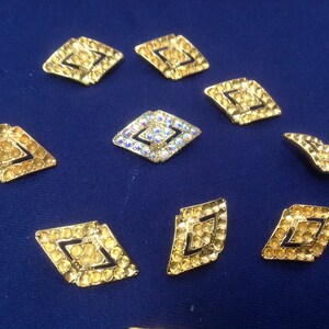 May include: Nine gold-toned diamond-shaped embellishments with clear rhinestones. Some of the rhinestones have an iridescent finish.