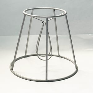 May include: A silver metal lampshade frame with a circular base and a teardrop-shaped wire loop.