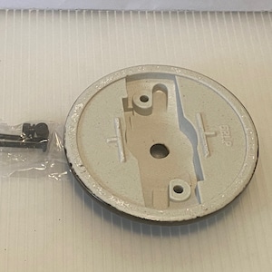 Pu&ograve; includere: Un apparecchio di illuminazione per soffitto bianco con una base rotonda e un bordo nero. La base ha un foro al centro e due piccoli fori sui lati. L'apparecchio viene fornito con due piccole viti nere.