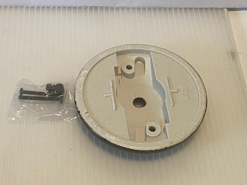 Pu&ograve; includere: Un apparecchio di illuminazione per soffitto bianco con una base rotonda e un bordo nero. La base ha un foro al centro e due piccoli fori sui lati. L'apparecchio viene fornito con due piccole viti nere.