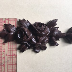 May include: A dark brown decorative trim with a repeating pattern of roses and leaves. The trim is made of a molded material and has a slightly textured surface.