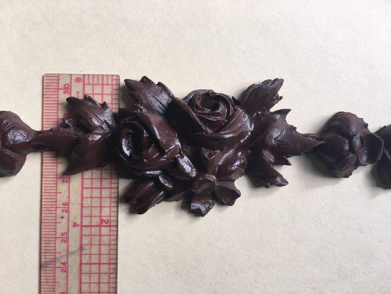 May include: A dark brown decorative trim with a repeating pattern of roses and leaves. The trim is made of a molded material and has a slightly textured surface.