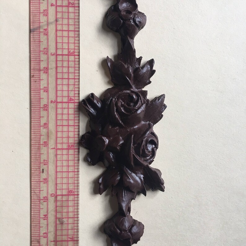 May include: A dark brown, ornate, wooden rose design with leaves. The design is approximately 7 inches tall.