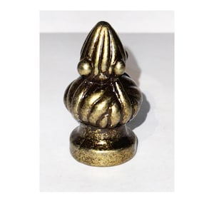 Puede incluir: Un remate de metal dorado con un diseño detallado y ornamentado. El remate tiene una parte superior puntiaguda y una base redondeada.