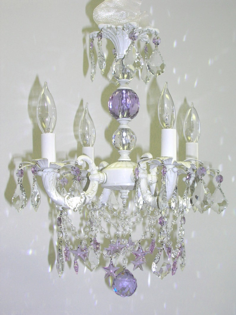 May include: White chandelier with crystal and purple glass accents. The chandelier has four candle-style light bulbs and a decorative top.