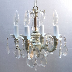 May include: A white and gold chandelier with crystal drops. The chandelier has four lights and a simple design.
