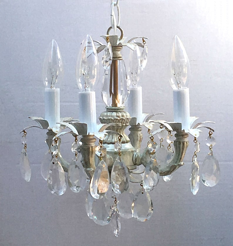 May include: A white and gold chandelier with crystal drops. The chandelier has four lights and a simple design.