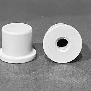 May include: Two white ceramic knobs with a round shape. One knob has a hole in the centre, while the other has a flat top.