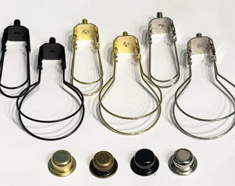 Puede incluir: Un conjunto de seis soportes metálicos para pantallas de lámpara en acabados negro, dorado y plateado, cada uno con un marco de alambre en forma de U y un tornillo de montaje superior. Cuatro remates metálicos circulares se alinean en la parte inferior.