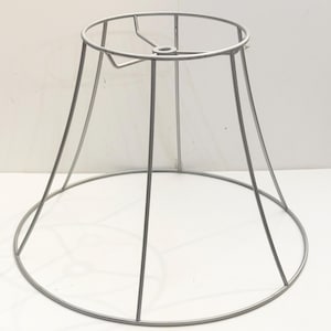 May include: A silver metal lampshade frame. The frame is circular and has a flared shape. It is designed to hold a lampshade.