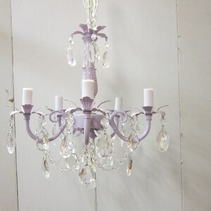 May include: A lavender-colored chandelier with crystal drops. The chandelier has five lights and a decorative floral design.