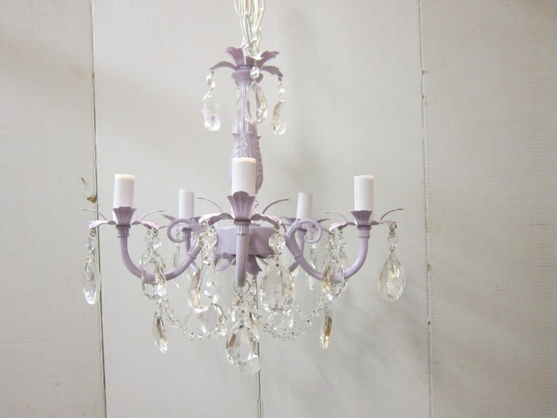 May include: A lavender-colored chandelier with crystal drops. The chandelier has five lights and a decorative floral design.