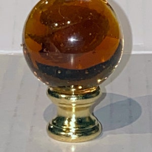 May include: A round amber glass lamp finial with a gold metal base.