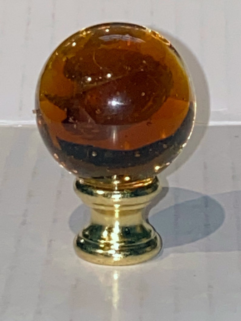 May include: A round amber glass lamp finial with a gold metal base.