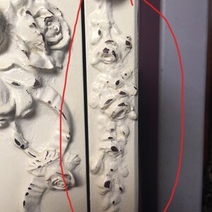 May include: White painted wooden cabinet with ornate floral carvings. The cabinet has a distressed finish and a decorative floral design on the side.