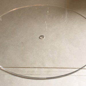 May include: A clear, circular acrylic disc with a small, centered hole. The transparent material allows light to pass through, and the smooth edges create a clean, modern aesthetic. This disc is suitable for various craft and design projects.