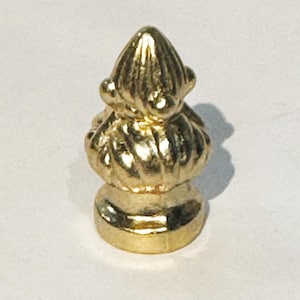 May include: A gold metal finial with a decorative, ornate design. The finial has a rounded base and a pointed top.