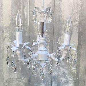 May include: White chandelier with crystal drops and three candle-style light bulbs.