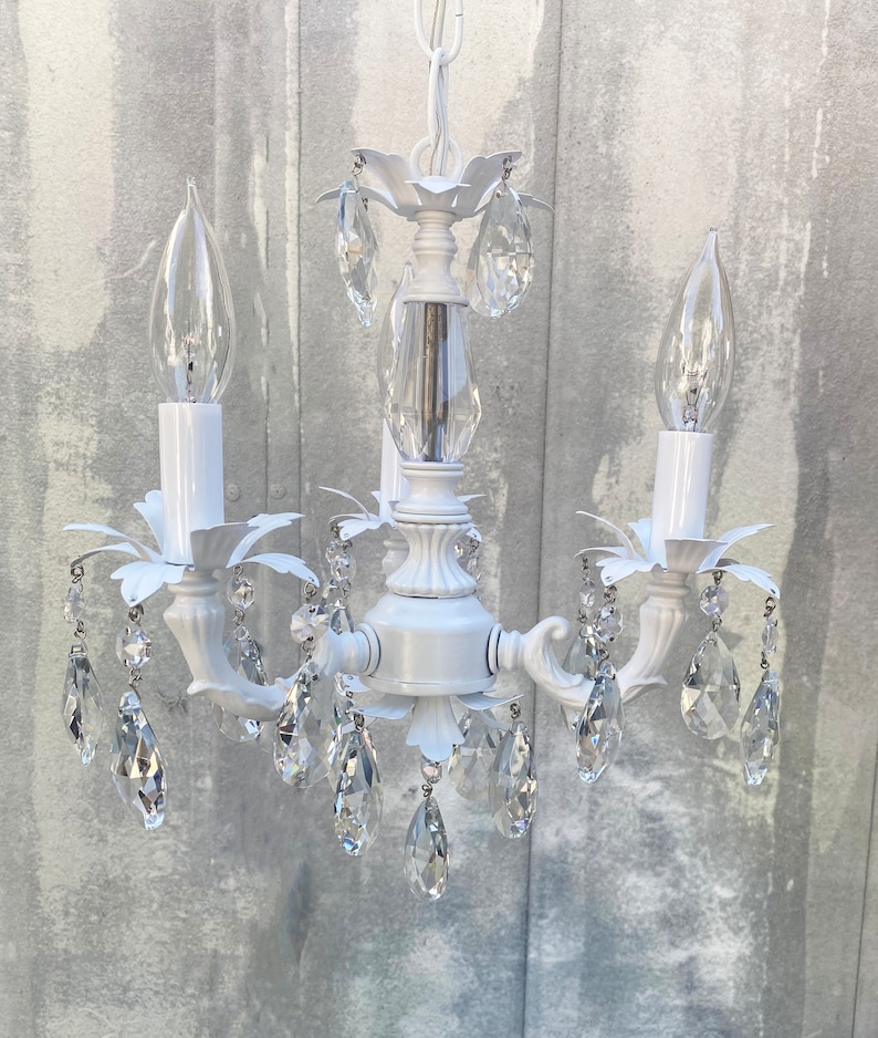 May include: White chandelier with crystal drops and three candle-style light bulbs.