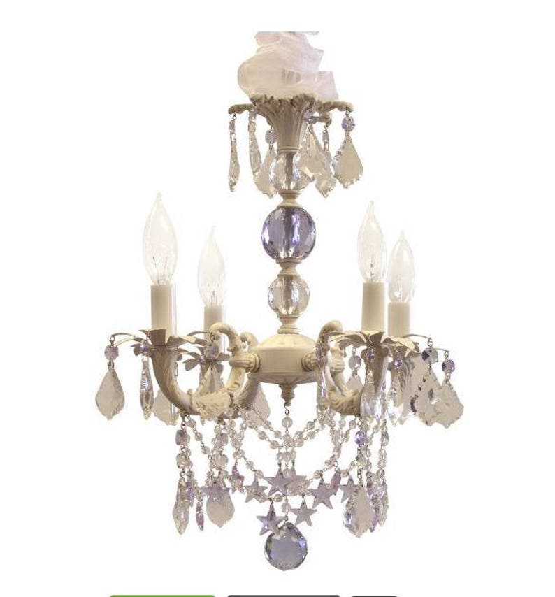 May include: A white chandelier with crystal drops and star accents. The chandelier has five lights and a white fabric shade.