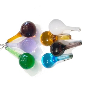 May include: A set of eight glass teardrop ornaments in various colors, including purple, green, blue, brown, white, and orange. The ornaments have a teardrop shape with a small, pointed tip and a larger, rounded bottom.