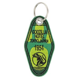 Puede incluir: Llavero verde y amarillo Godzilla Hotel Tokio, Japón 1954. El llavero tiene un borde negro y un llavero plateado. El diseño presenta un gráfico de Godzilla.