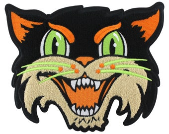 May include: An embroidered patch of a cat's face, featuring black fur, orange ears, green eyes and a wide, toothy grin.
